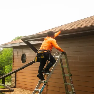 Roofer on a ladder working at the roof edge of a home